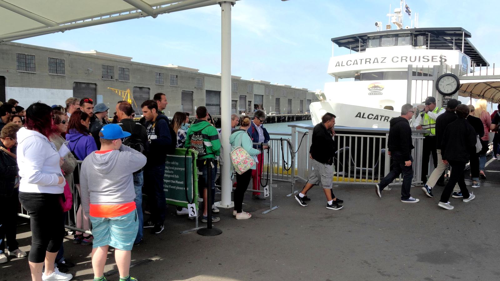 Visitors queueing under the canopy at Pier 33 Alcatraz Landing in San Francisco as an Alcatraz Cruises ferry waits at the dock